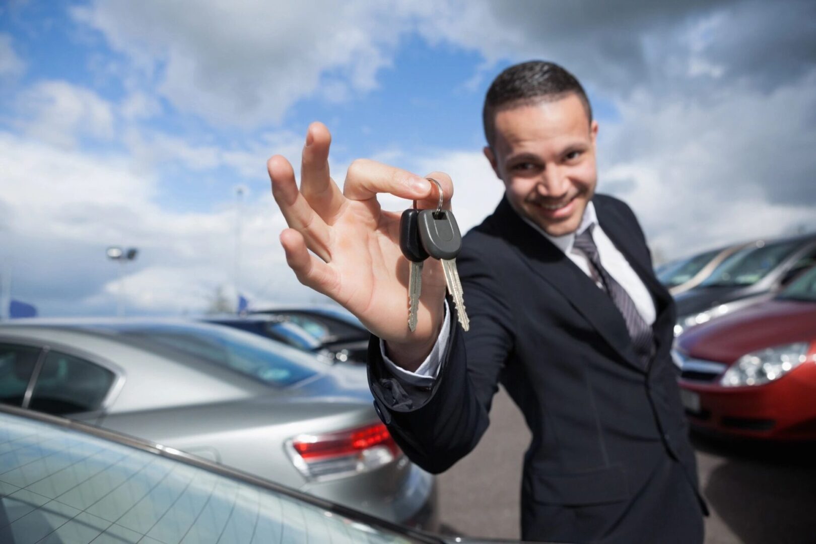 A man holding up his car keys in front of some cars.