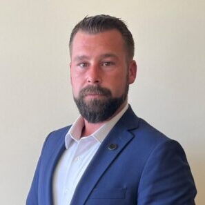 A man in a suit and beard standing against a wall.